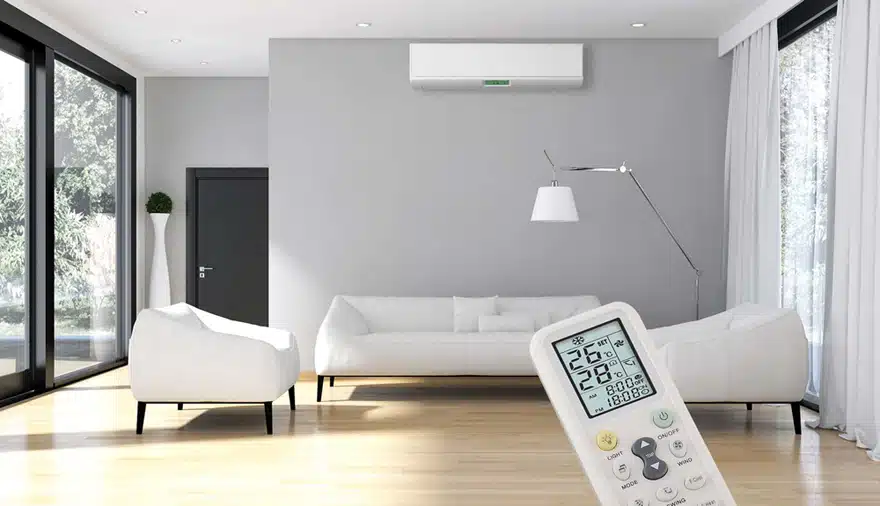 Bright modern living room featuring white furniture, a wall-mounted air conditioner, and a remote control in the foreground.